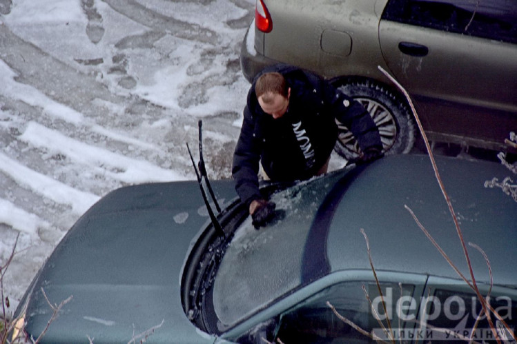 Человек чистит от льда стекло автомобиля